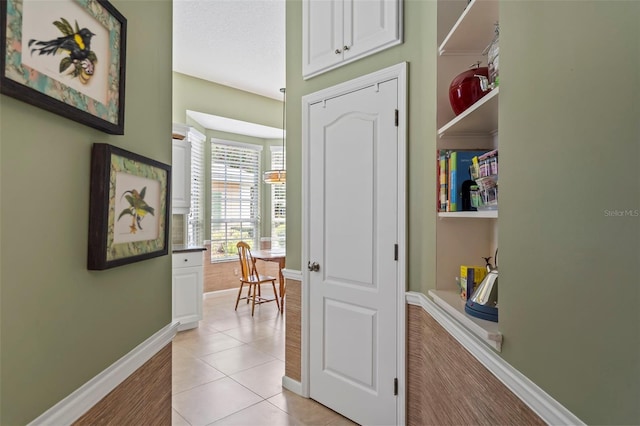 hallway with a textured ceiling, light tile patterned flooring, and baseboards