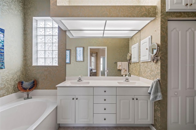 bathroom featuring a bath, wallpapered walls, double vanity, and a sink