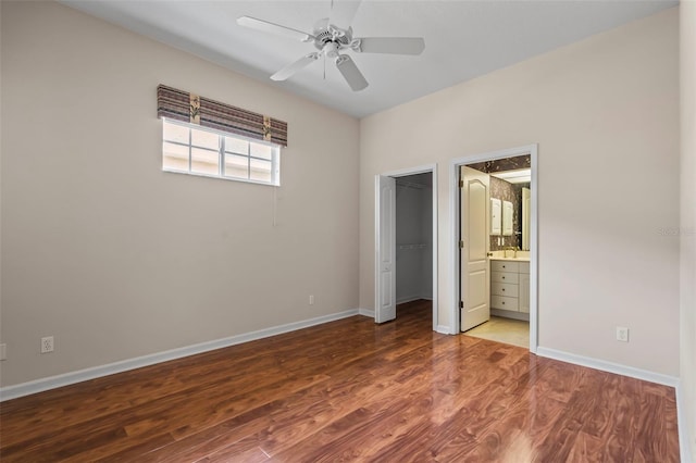 unfurnished bedroom featuring a closet, a spacious closet, ensuite bath, wood finished floors, and baseboards