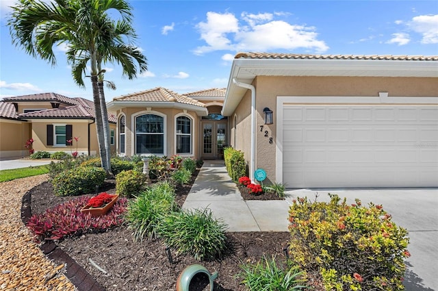 mediterranean / spanish home featuring a garage, a tiled roof, concrete driveway, and stucco siding