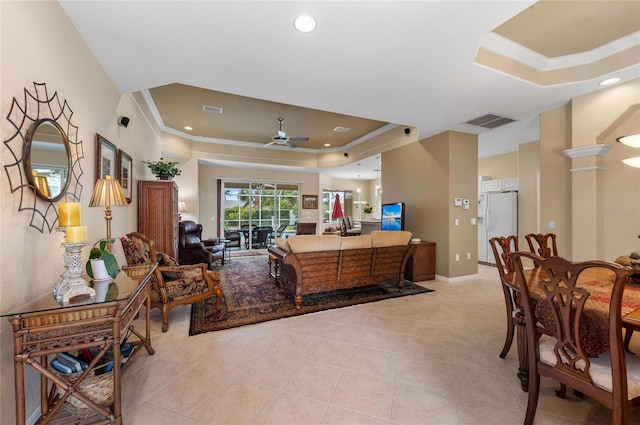 living area with visible vents, a tray ceiling, a ceiling fan, and ornamental molding