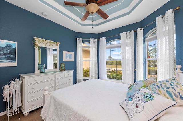 bedroom with a tray ceiling, dark colored carpet, and a ceiling fan