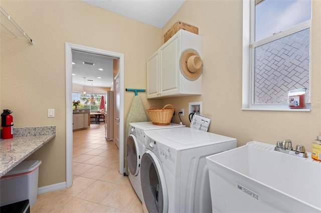 laundry area featuring light tile patterned floors, a sink, baseboards, cabinet space, and washing machine and clothes dryer