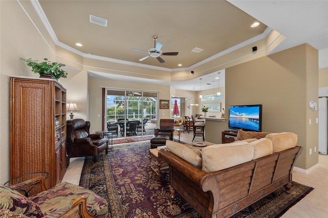 living area with a tray ceiling, visible vents, ceiling fan, and crown molding