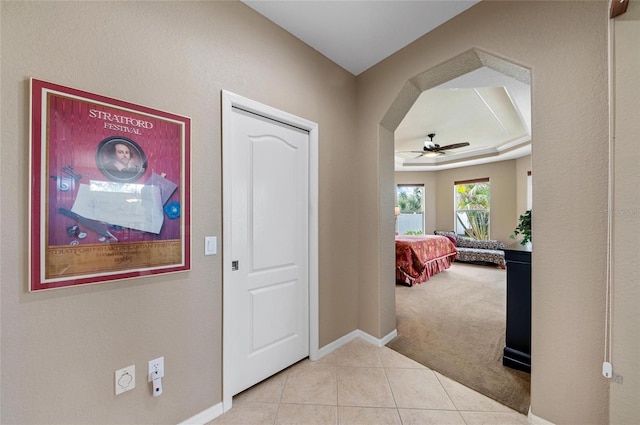 foyer entrance with arched walkways, light tile patterned floors, light carpet, baseboards, and a tray ceiling