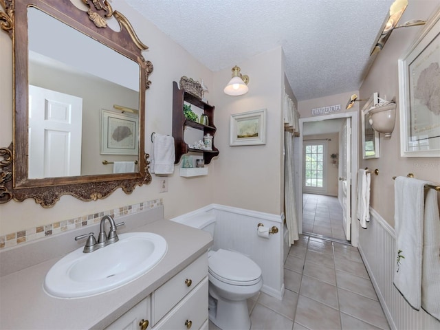 full bathroom featuring a wainscoted wall, toilet, vanity, tile patterned floors, and a textured ceiling