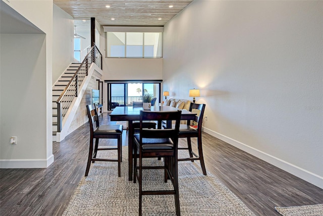 dining area featuring stairs, wood finished floors, a towering ceiling, and baseboards