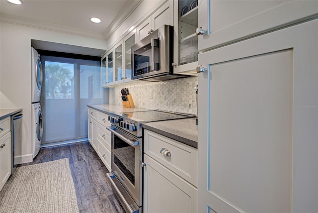 kitchen featuring decorative backsplash, stacked washer and clothes dryer, ornamental molding, dark wood-type flooring, and stainless steel appliances