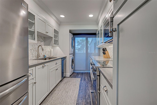 kitchen with stacked washer and dryer, appliances with stainless steel finishes, dark wood-type flooring, ornamental molding, and a sink