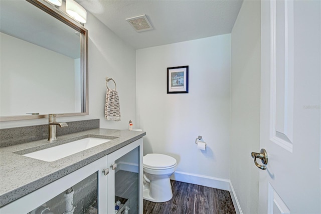 bathroom featuring baseboards, visible vents, toilet, wood finished floors, and vanity