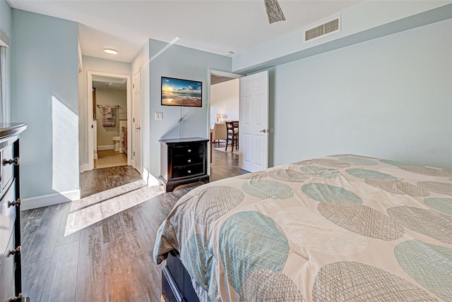 bedroom with connected bathroom, wood finished floors, visible vents, and baseboards