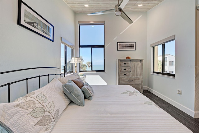 bedroom with dark wood-type flooring, baseboards, multiple windows, and a high ceiling