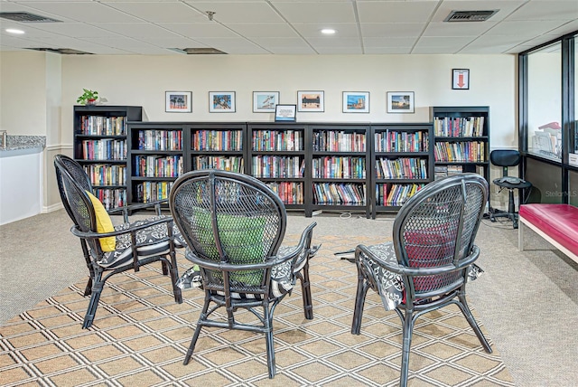 office space featuring a paneled ceiling, wall of books, carpet flooring, and visible vents