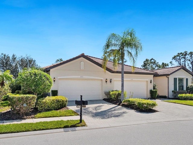 mediterranean / spanish home featuring a garage, a tiled roof, decorative driveway, and stucco siding