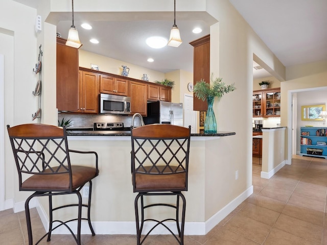 kitchen featuring a breakfast bar area, a peninsula, appliances with stainless steel finishes, backsplash, and dark countertops