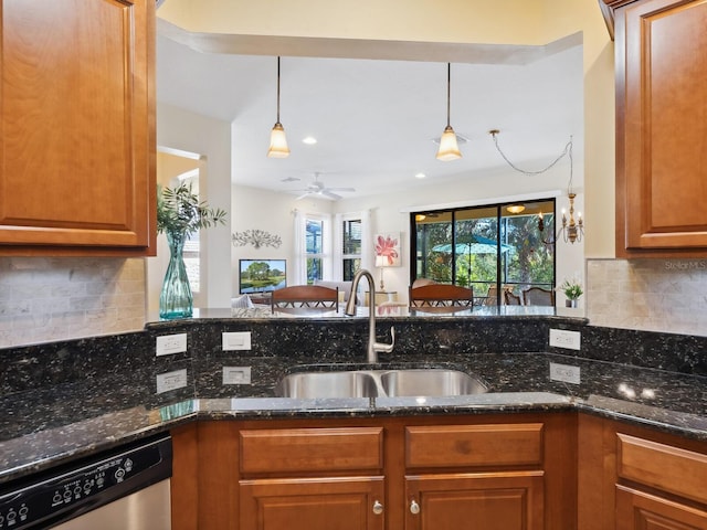 kitchen with brown cabinetry, backsplash, dark stone countertops, stainless steel dishwasher, and a sink