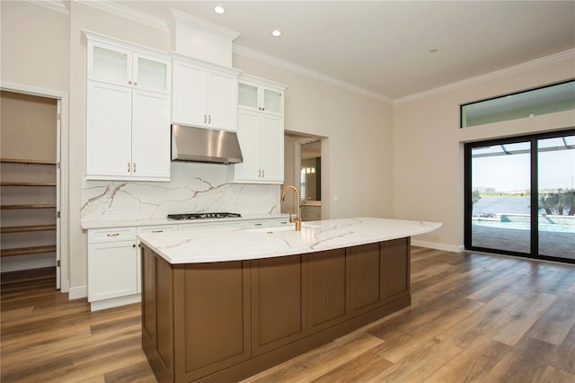 kitchen with light stone counters, gas cooktop, under cabinet range hood, a sink, and white cabinetry