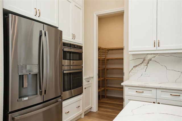 kitchen with white cabinets, light stone countertops, stainless steel appliances, light wood-style floors, and backsplash