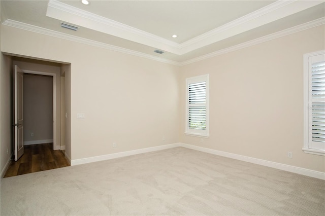 carpeted empty room featuring ornamental molding, a raised ceiling, and baseboards