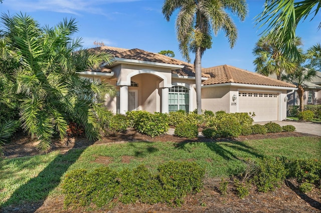 mediterranean / spanish house featuring a garage, a tile roof, driveway, stucco siding, and a front lawn