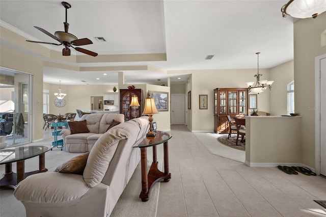 living area featuring ceiling fan with notable chandelier, visible vents, baseboards, ornamental molding, and a tray ceiling