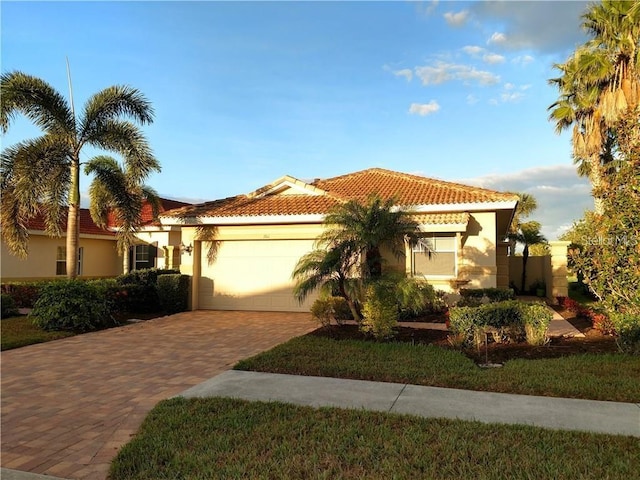 mediterranean / spanish house featuring decorative driveway, a tile roof, an attached garage, and stucco siding