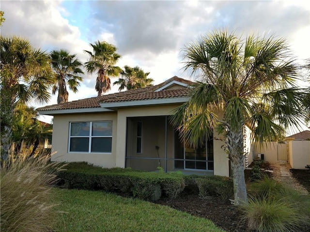 rear view of house featuring a tile roof, fence, and stucco siding