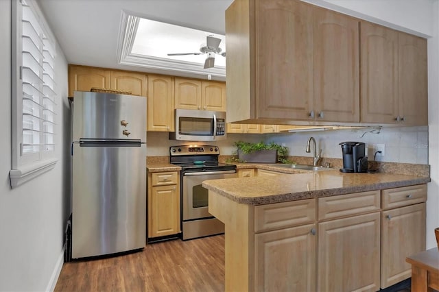 kitchen with light wood finished floors, a ceiling fan, stainless steel appliances, light brown cabinets, and a sink