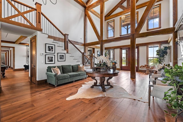 living room featuring wood-type flooring, stairs, baseboards, and beam ceiling