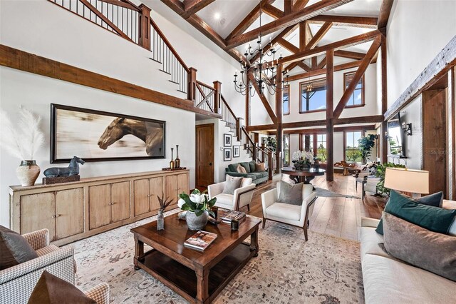 living area with a notable chandelier, stairs, light wood-style floors, high vaulted ceiling, and beam ceiling