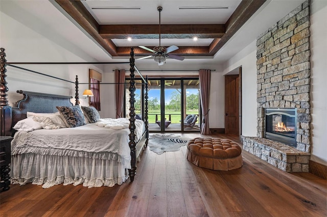 bedroom featuring access to outside, beamed ceiling, hardwood / wood-style floors, and a stone fireplace