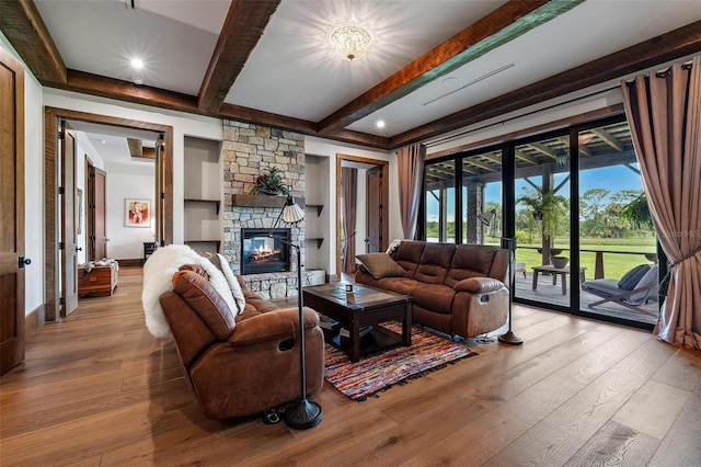 living room with a stone fireplace, beam ceiling, and hardwood / wood-style flooring