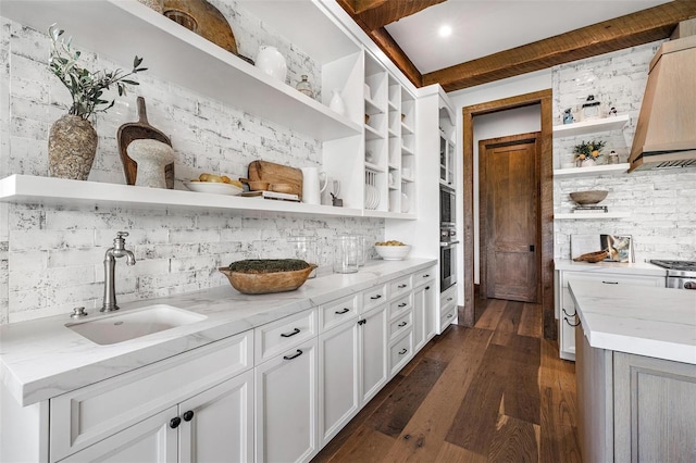 kitchen with light stone counters, a sink, stainless steel oven, open shelves, and dark wood finished floors