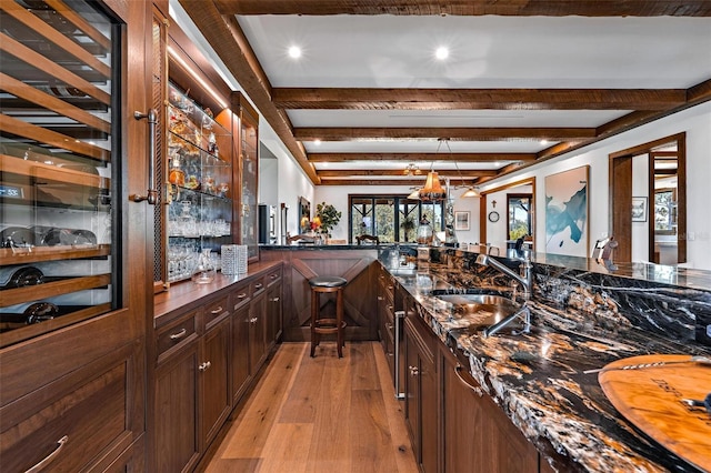 bar with indoor wet bar, a sink, light wood-style flooring, and beamed ceiling