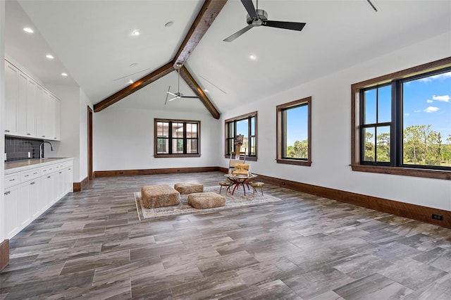 unfurnished living room featuring lofted ceiling with beams, ceiling fan, wood finished floors, and baseboards