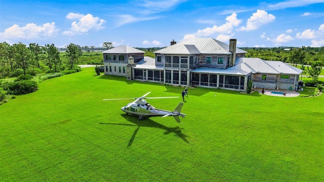 rear view of property featuring a lawn, metal roof, a chimney, and a sunroom