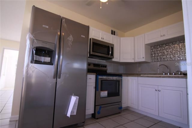 kitchen featuring light tile patterned floors, stainless steel appliances, a sink, white cabinets, and tasteful backsplash