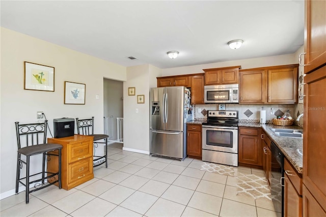 kitchen with visible vents, light tile patterned flooring, appliances with stainless steel finishes, brown cabinets, and backsplash