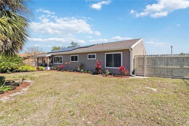 back of house with a lawn, fence, roof mounted solar panels, and stucco siding