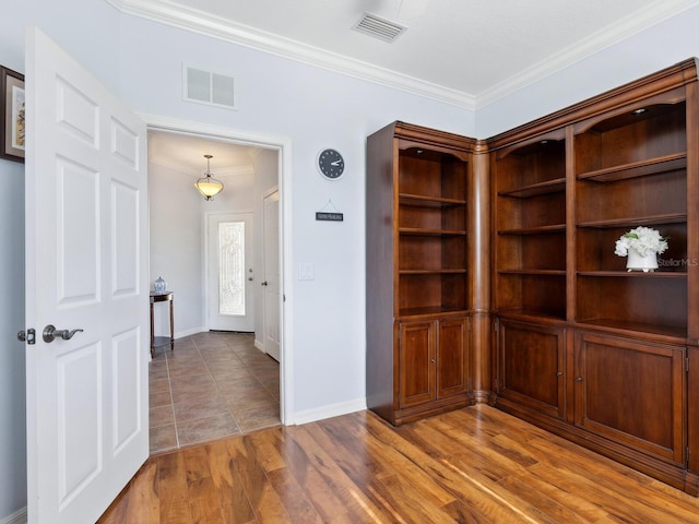 empty room with baseboards, visible vents, crown molding, and wood finished floors