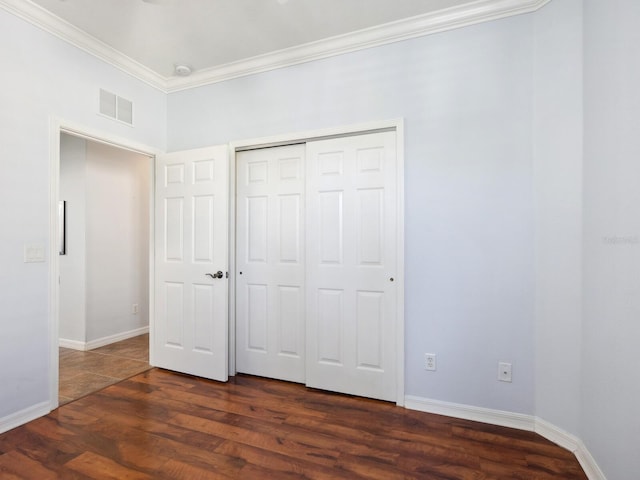 unfurnished bedroom featuring baseboards, visible vents, dark wood-style floors, ornamental molding, and a closet