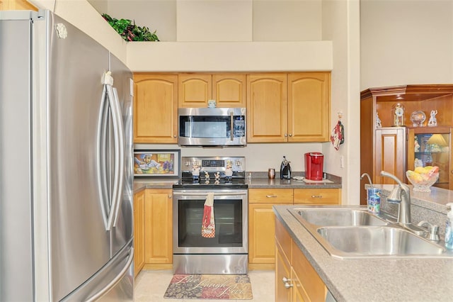 kitchen with light tile patterned floors, light brown cabinetry, appliances with stainless steel finishes, and a sink