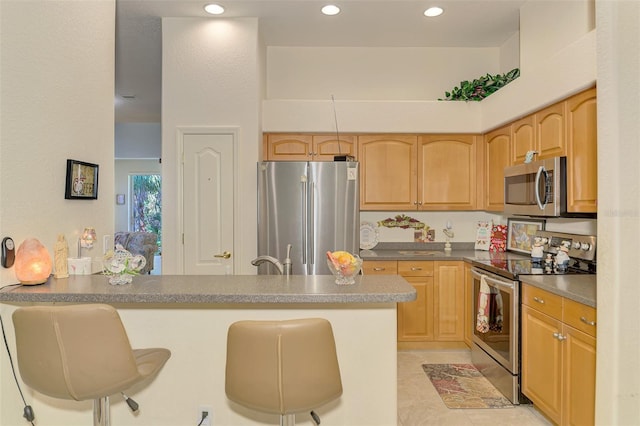 kitchen with a breakfast bar area, recessed lighting, dark countertops, appliances with stainless steel finishes, and a peninsula