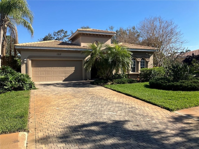 mediterranean / spanish home with a garage, a tile roof, decorative driveway, a front lawn, and stucco siding