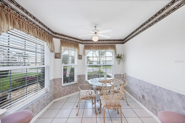 dining space with a wainscoted wall, ceiling fan, light tile patterned floors, and wallpapered walls