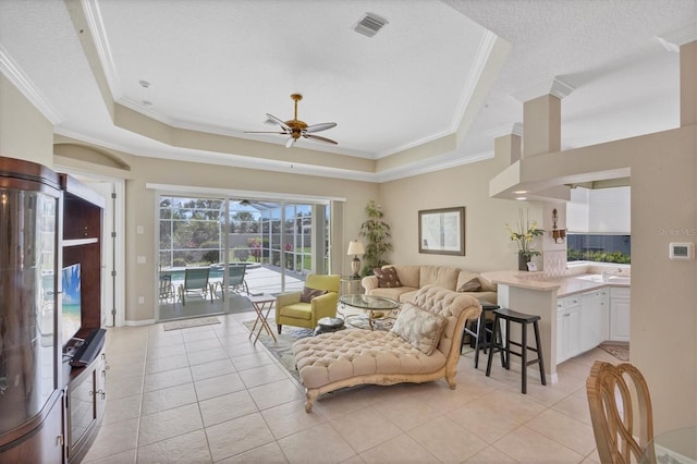 living room with light tile patterned floors, visible vents, a tray ceiling, and ornamental molding