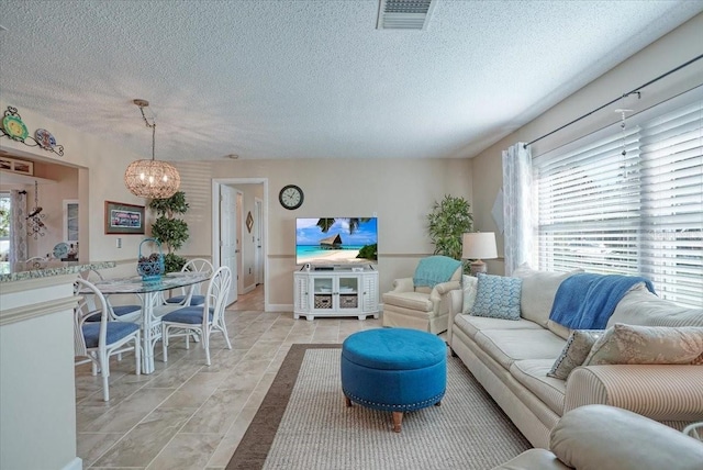 living area featuring light tile patterned floors, a notable chandelier, a textured ceiling, and visible vents