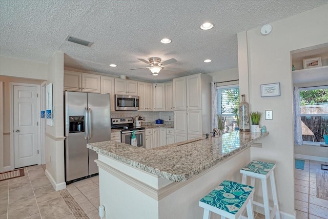 kitchen with a kitchen bar, visible vents, backsplash, stainless steel appliances, and a peninsula