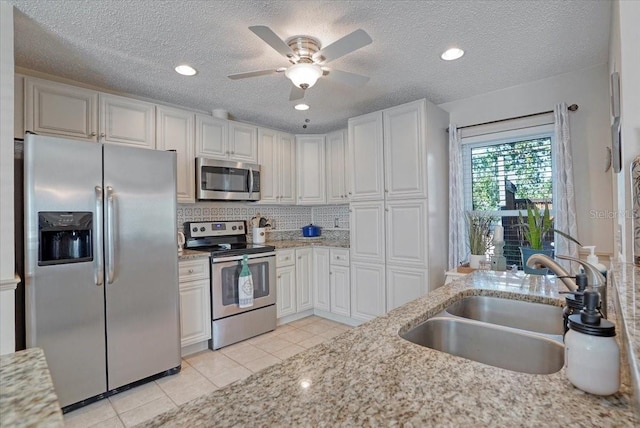 kitchen with a sink, light stone counters, appliances with stainless steel finishes, and light tile patterned floors