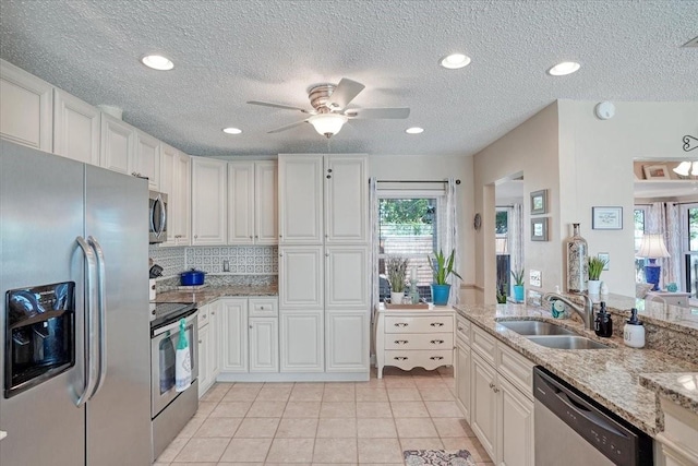 kitchen with a sink, appliances with stainless steel finishes, light tile patterned flooring, and white cabinetry